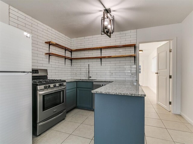 kitchen with stainless steel range with gas cooktop, a sink, light tile patterned flooring, freestanding refrigerator, and open shelves