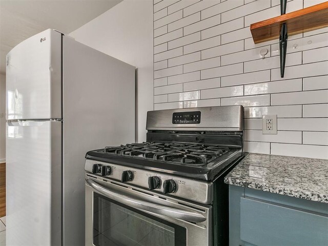 kitchen featuring freestanding refrigerator, stone counters, gas stove, and tasteful backsplash