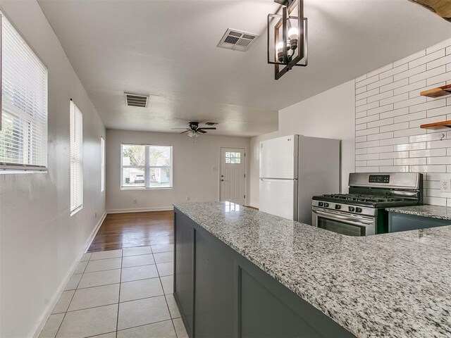 kitchen with light stone counters, visible vents, light tile patterned floors, freestanding refrigerator, and gas stove