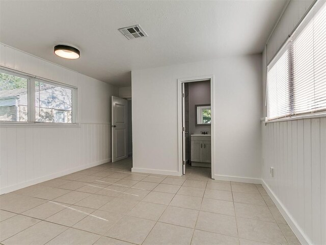 interior space with wainscoting, visible vents, light tile patterned floors, and a healthy amount of sunlight