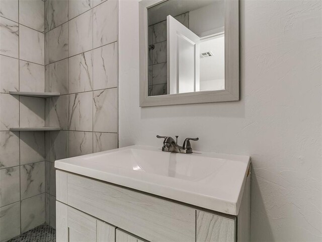 bathroom with visible vents, vanity, and tiled shower