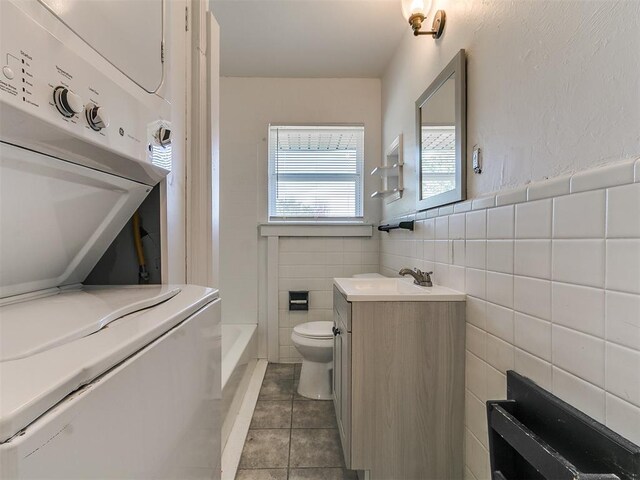 full bathroom with toilet, tile walls, stacked washer / dryer, tile patterned flooring, and vanity
