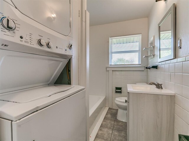bathroom with vanity, stacked washing maching and dryer, tile walls, toilet, and tile patterned flooring