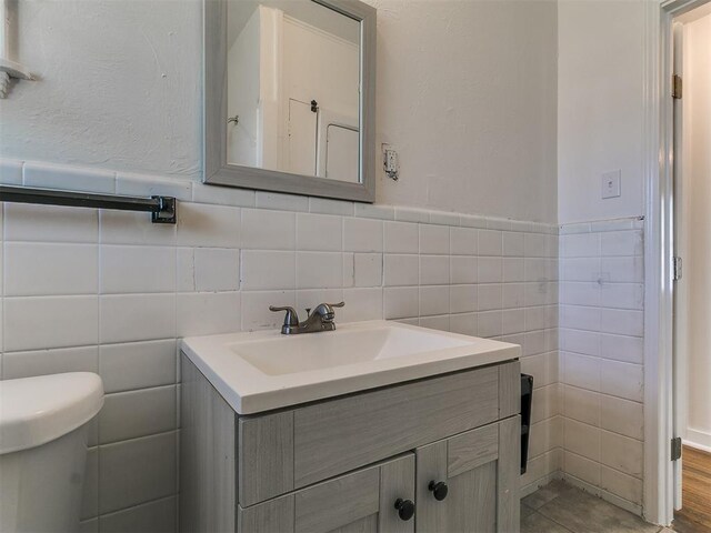 bathroom with wainscoting, toilet, vanity, and tile walls