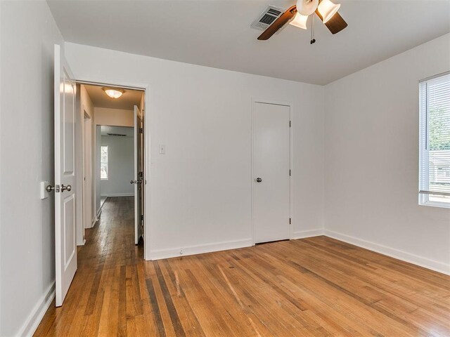 unfurnished bedroom with hardwood / wood-style flooring, baseboards, a ceiling fan, and visible vents