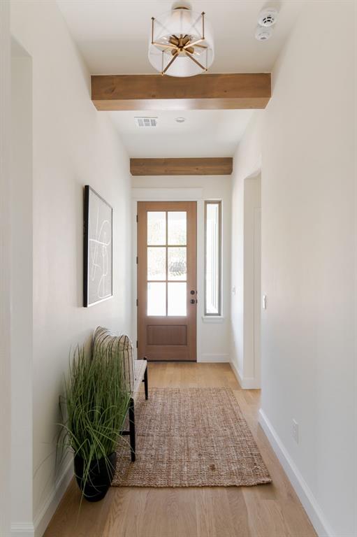 doorway to outside with beamed ceiling, light wood-style flooring, baseboards, a notable chandelier, and visible vents