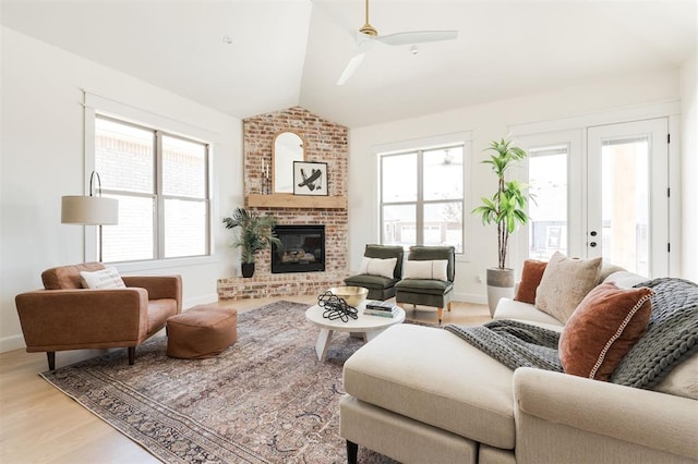 living area with vaulted ceiling, baseboards, light wood-style floors, a ceiling fan, and a brick fireplace