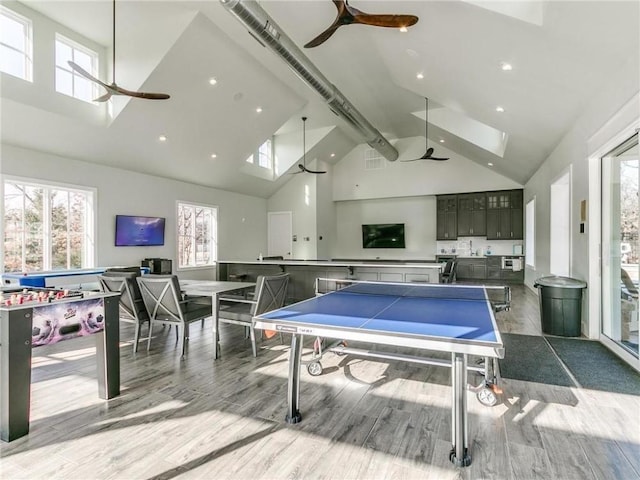 rec room with a skylight, a ceiling fan, wood finished floors, and high vaulted ceiling