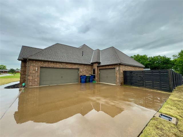 exterior space featuring roof with shingles, an attached garage, fence, and brick siding