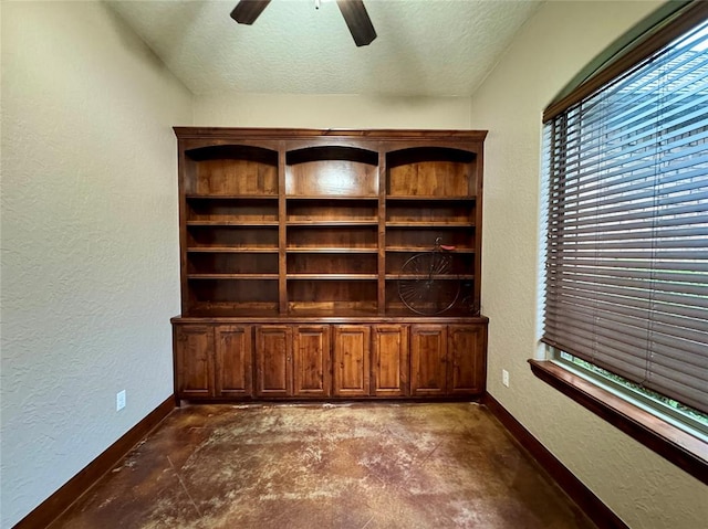 interior space featuring ceiling fan, a textured wall, unfinished concrete floors, baseboards, and a textured ceiling