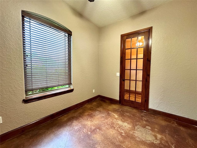 spare room with concrete floors, a textured wall, a textured ceiling, and baseboards