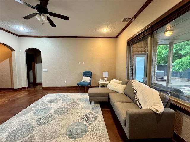 living area with a textured ceiling, a textured wall, visible vents, arched walkways, and ornamental molding