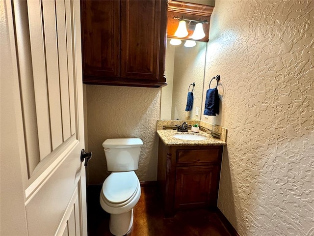 half bathroom featuring toilet, a textured wall, and vanity