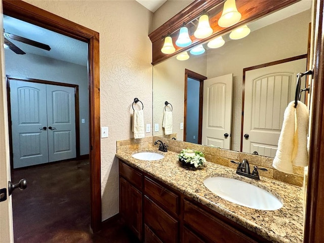 bathroom featuring a ceiling fan, a sink, a textured wall, and double vanity