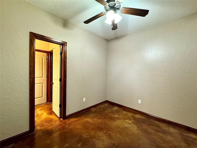spare room featuring concrete floors, a ceiling fan, a textured wall, baseboards, and a textured ceiling
