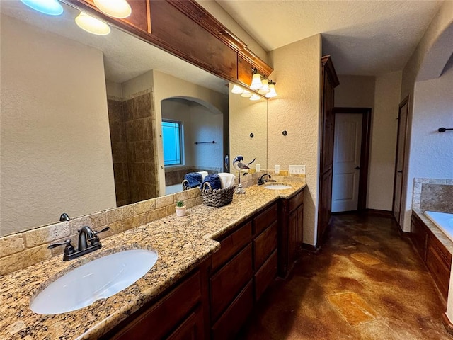 full bathroom featuring double vanity, finished concrete flooring, a bath, a textured wall, and a sink