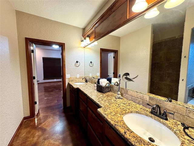 bathroom with double vanity, a sink, a textured wall, and baseboards