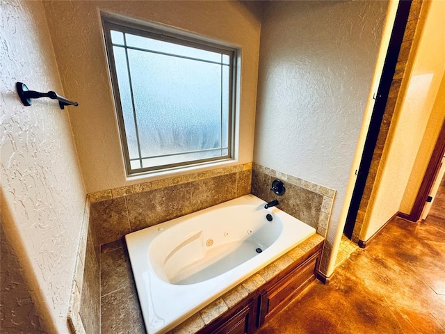 bathroom with concrete floors, a textured wall, and a jetted tub