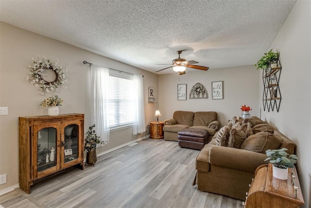 living area featuring light wood-style flooring, baseboards, a textured ceiling, and a ceiling fan