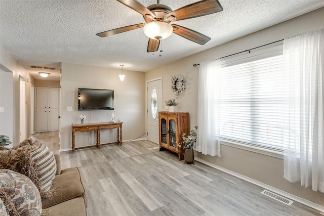 living room with light wood-style flooring, visible vents, a textured ceiling, and a healthy amount of sunlight