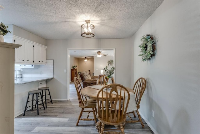 dining room featuring light wood-style flooring, a textured ceiling, baseboards, and ceiling fan