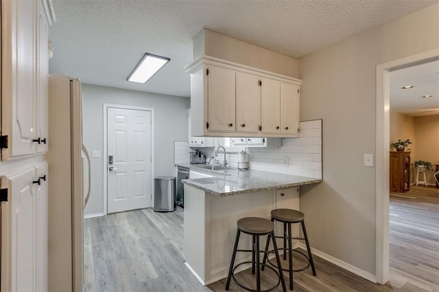 kitchen with light wood finished floors, a peninsula, a sink, freestanding refrigerator, and white cabinetry