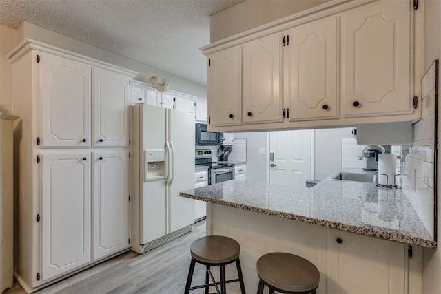 kitchen featuring a sink, black microwave, white fridge with ice dispenser, white cabinets, and a peninsula