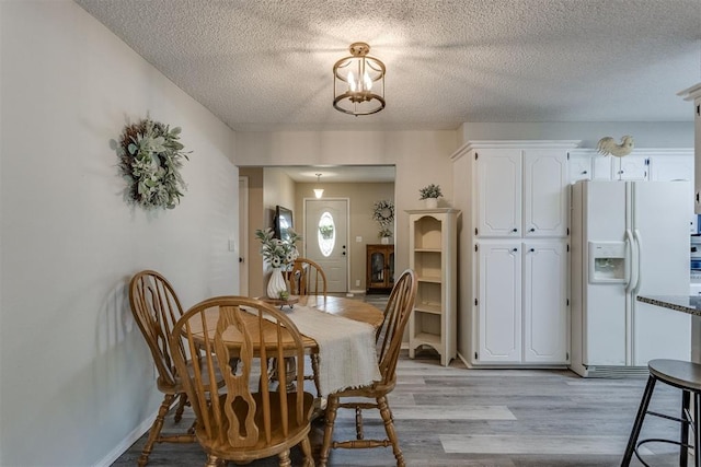 dining area with baseboards, a notable chandelier, a textured ceiling, and light wood finished floors