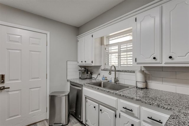 kitchen featuring a sink, decorative backsplash, dishwasher, light wood-style flooring, and white cabinets
