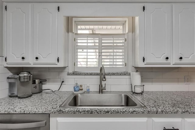 kitchen with white cabinets, stainless steel dishwasher, tasteful backsplash, and a sink