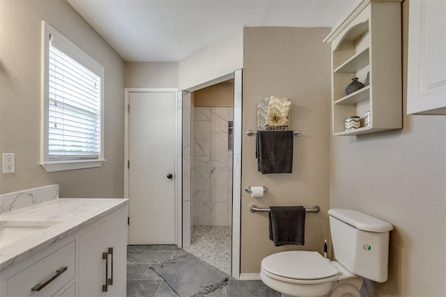 full bath with a marble finish shower, vanity, and toilet