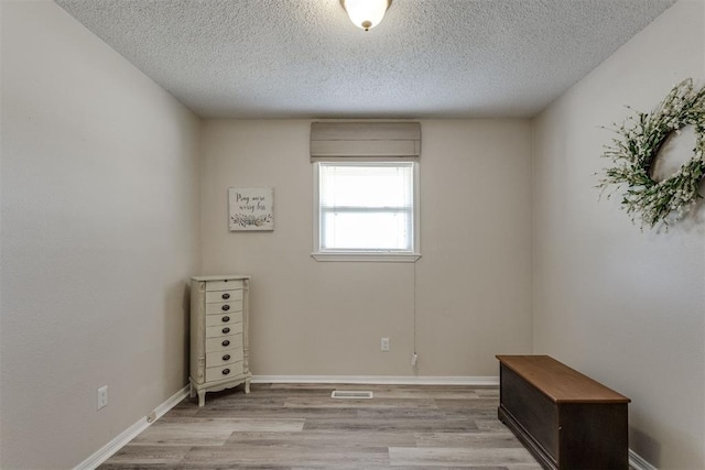 spare room featuring light wood-type flooring, a textured ceiling, baseboards, and visible vents