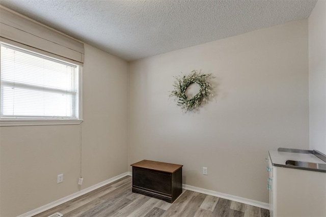 unfurnished room with baseboards, light wood-style floors, and a textured ceiling