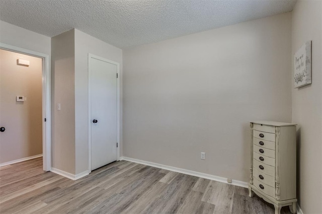 unfurnished bedroom with a textured ceiling, light wood finished floors, and baseboards