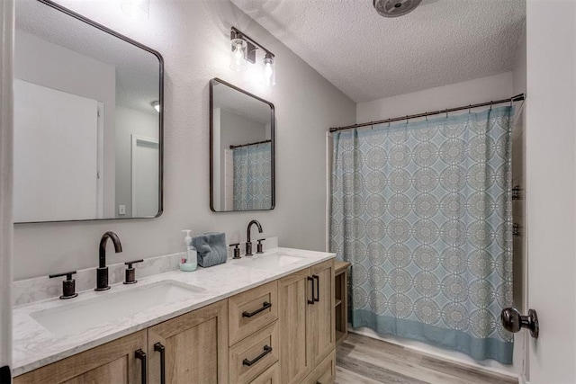full bathroom featuring wood finished floors, a sink, a textured ceiling, and double vanity