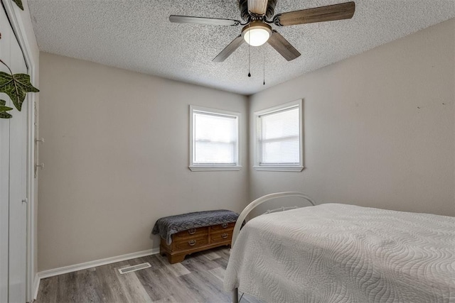 bedroom with a ceiling fan, a textured ceiling, light wood-type flooring, baseboards, and visible vents