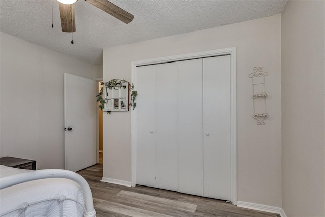 bedroom with light wood finished floors, a textured ceiling, baseboards, a ceiling fan, and a closet