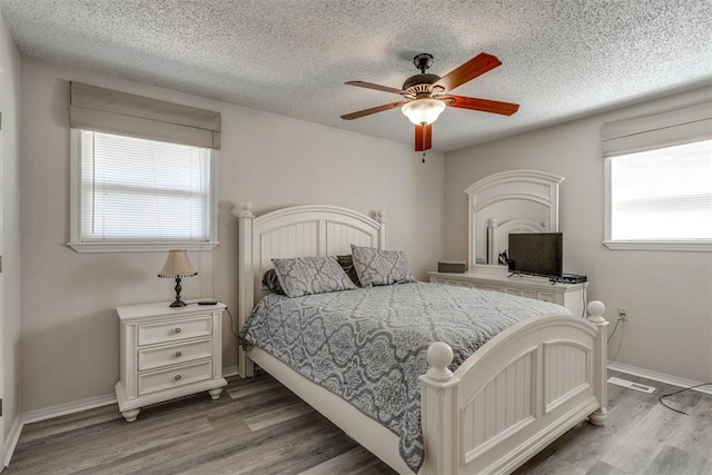 bedroom featuring wood finished floors, a textured ceiling, ceiling fan, baseboards, and visible vents