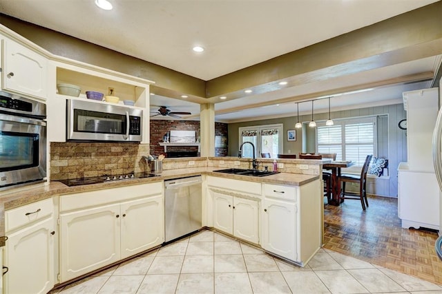kitchen with a sink, appliances with stainless steel finishes, a peninsula, a ceiling fan, and backsplash