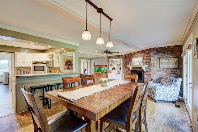 dining area with crown molding, ceiling fan, brick wall, and a fireplace