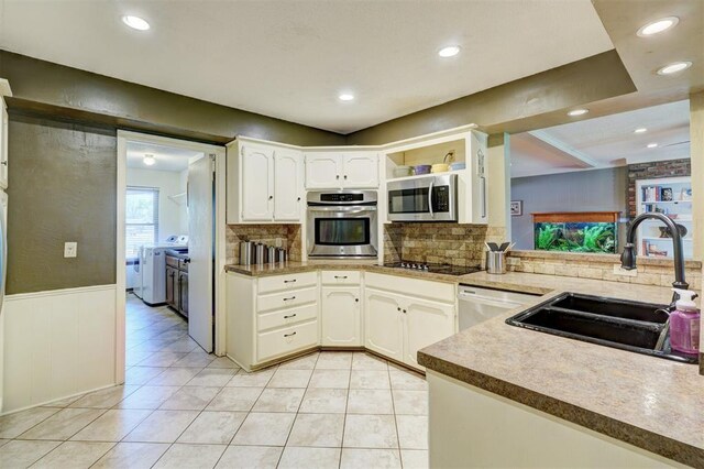 kitchen with a sink, appliances with stainless steel finishes, light tile patterned flooring, washer and dryer, and backsplash