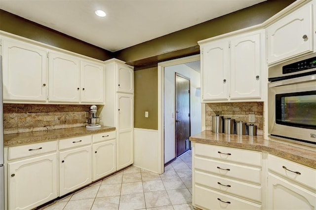 kitchen with decorative backsplash, wainscoting, light countertops, white cabinets, and stainless steel oven