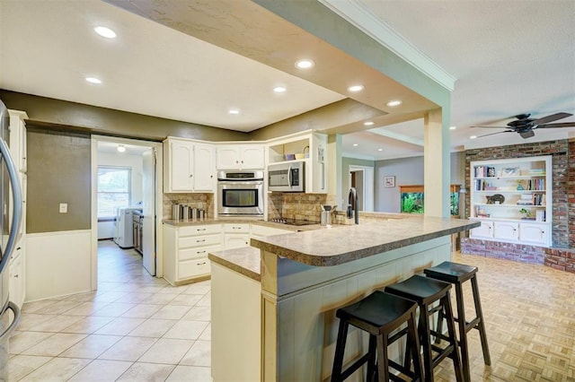 kitchen with washing machine and clothes dryer, appliances with stainless steel finishes, a kitchen bar, a peninsula, and backsplash