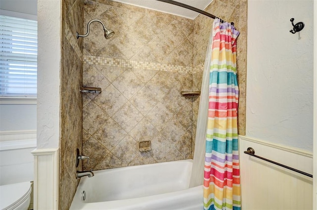 bathroom with shower / bath combo, a textured wall, toilet, and a wainscoted wall
