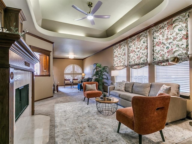 carpeted living room with a tray ceiling, baseboards, a ceiling fan, crown molding, and a fireplace