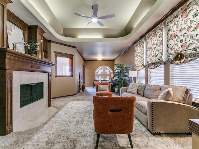 living area featuring a fireplace, a raised ceiling, a ceiling fan, and ornamental molding