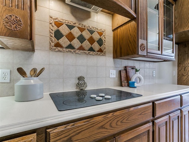 kitchen with glass insert cabinets, tasteful backsplash, light countertops, and black electric cooktop