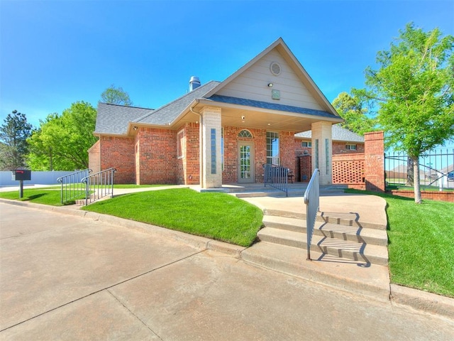 view of front facade featuring fence, a shingled roof, brick siding, and a front yard