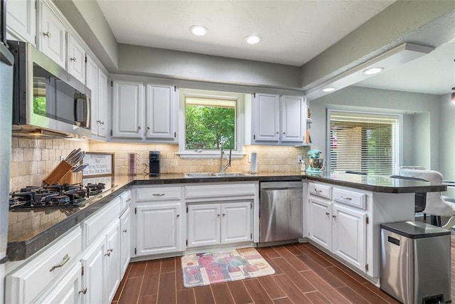 kitchen with a sink, appliances with stainless steel finishes, dark countertops, and a peninsula