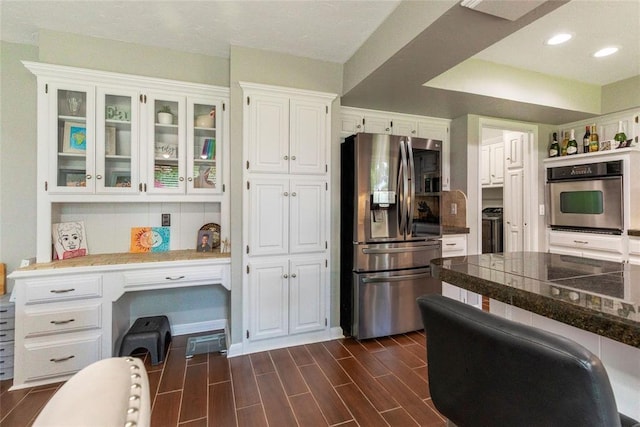 kitchen featuring appliances with stainless steel finishes, built in desk, white cabinets, dark wood-style floors, and glass insert cabinets